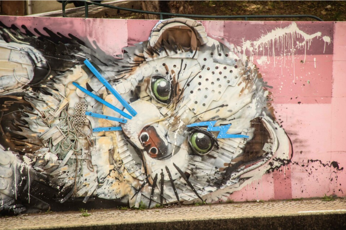 Large street art sculpture titled “Half Weasel” by Bordalo II in Lisbon, created from discarded materials like metal scraps, old plastic, and car parts, depicting the head and body of a weasel emerging from a wall.